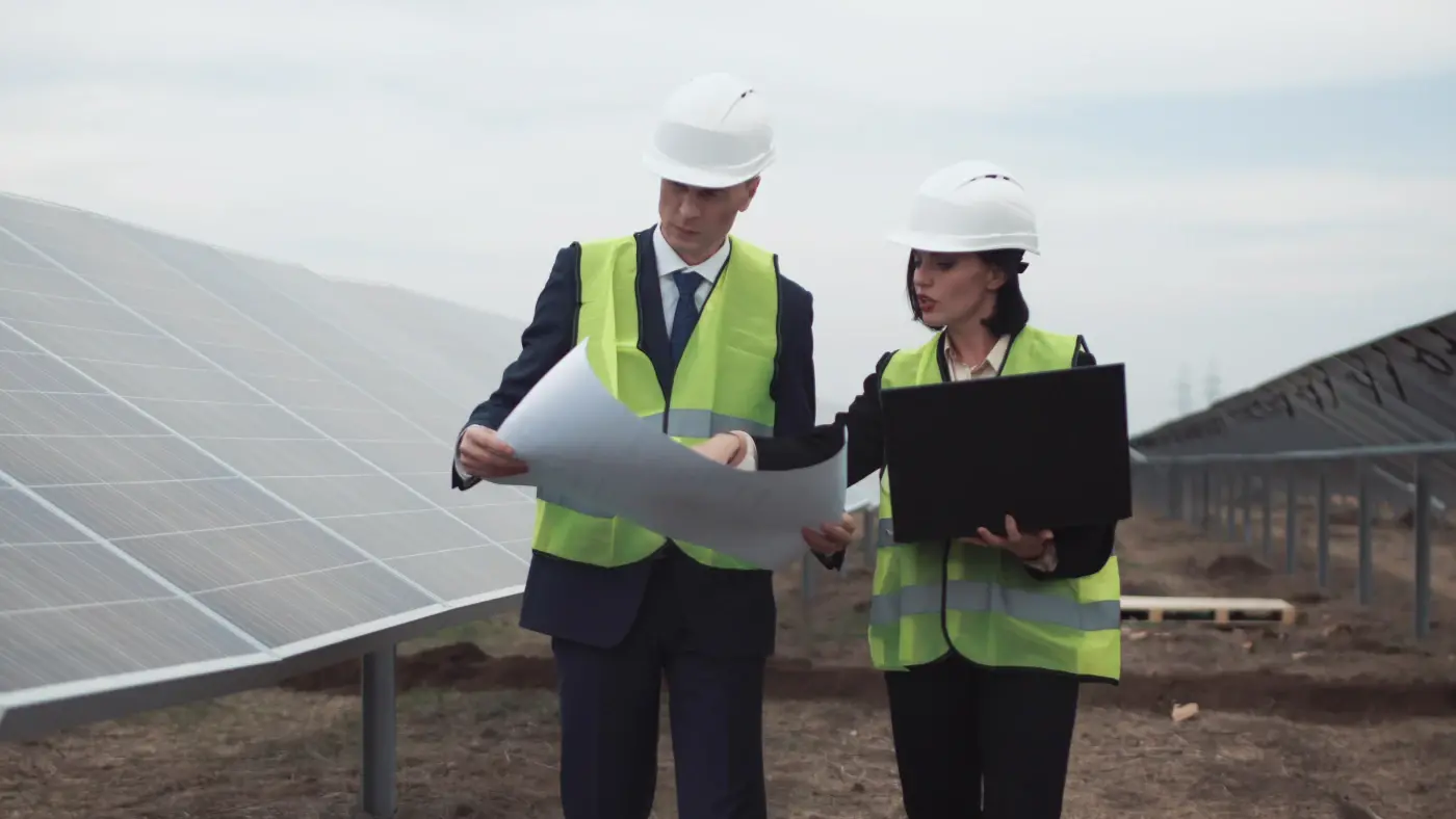 homme avec une fiche technique et femme discutent avec des panneaux solaires en arrière-plan