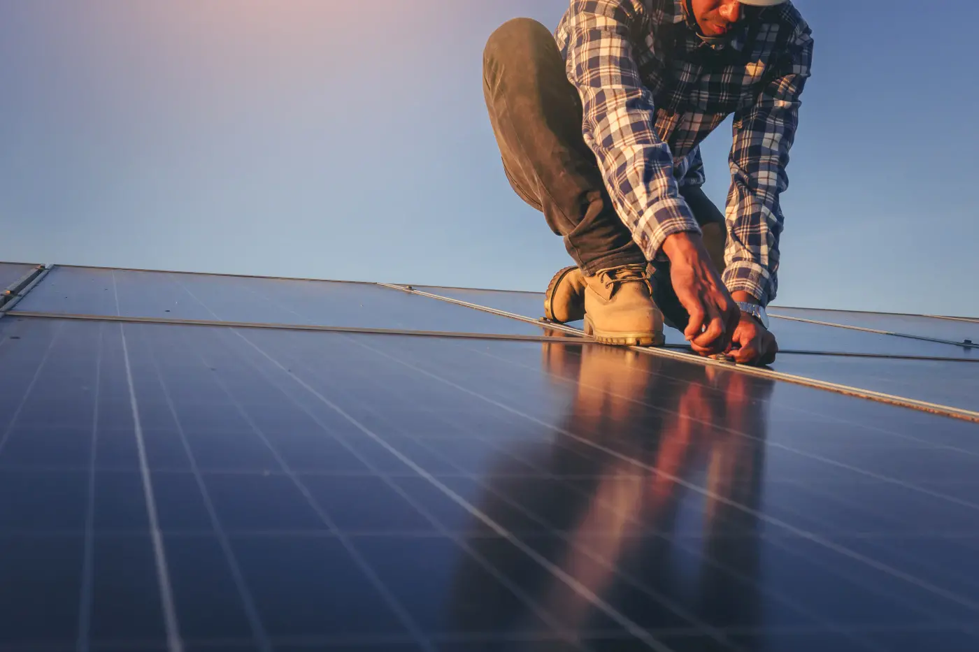 technicien en train de fixer plusieurs panneaux solaires sur un toit