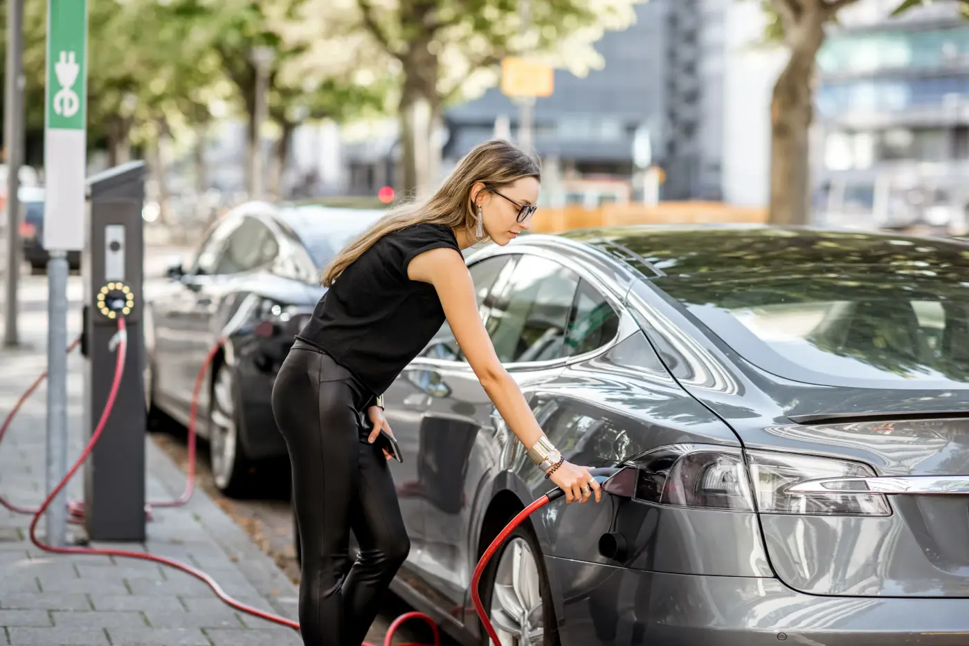 une jeune femme qui recharge sa voiture électrique sur une borne de recharge pour voiture électrique