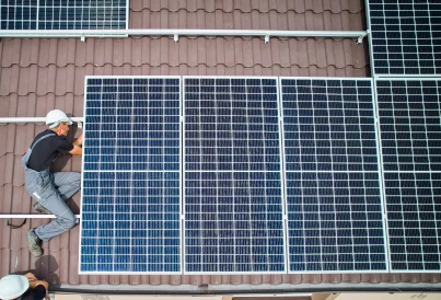 monsieur portant un casque de chantier blanc qui installe des panneaux solaire sur un toit marron